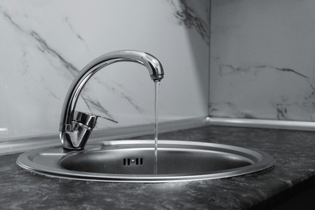 Home Chrome faucet with running water in a modern kitchen with marble countertop.
